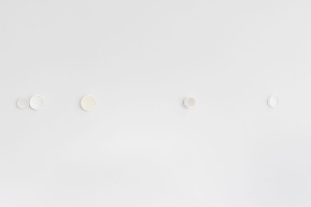 Imagen: inter.densidad, 2025. Cinco tapones de plástico blanco están fijados a una pared blanca, a una distancia casi equidistante entre sí. Imagen cortesía de Gallery 400.