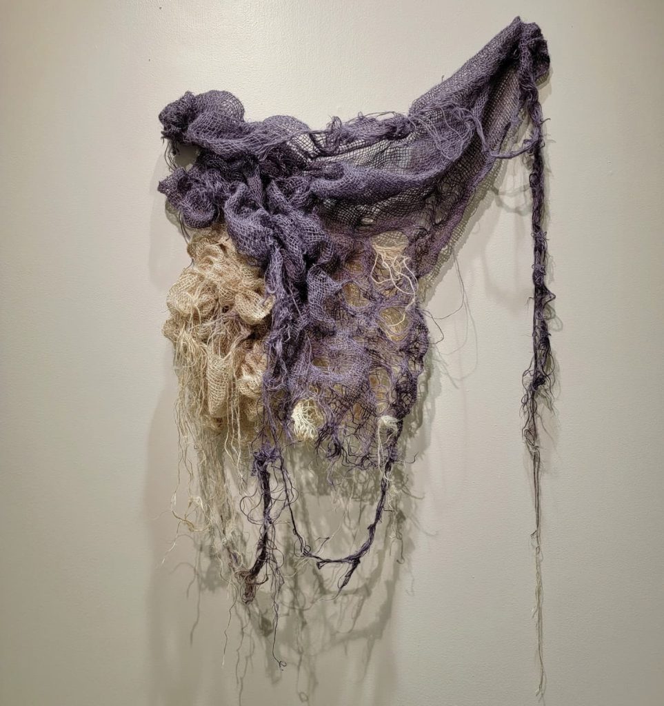 No Strings Attached art series by by Allena Marie Brazier, burlap, 2023. A burlap piece bleached and dyed with black beans is gathered in bunches and hanging on the gallery wall. Image courtesy of the artist.