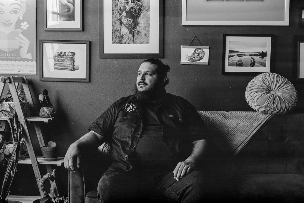 Black and white captures of photographer Carlos Martinez sitting in his studio and holding his guitar. Photos by Genesis Falls.