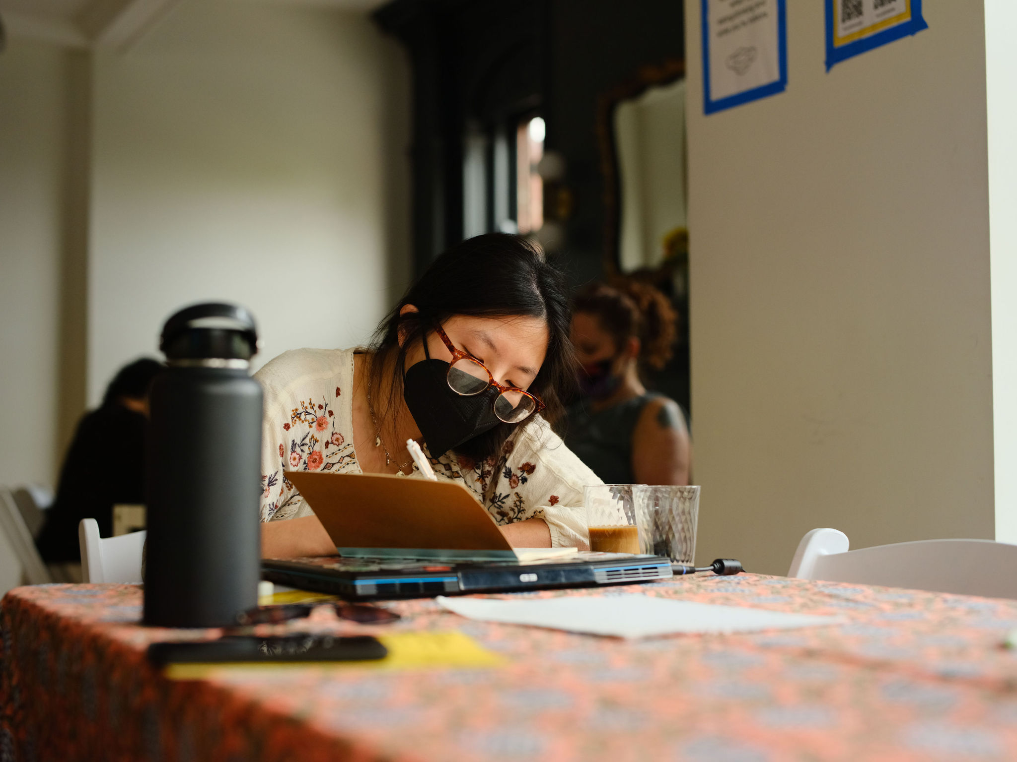 Image: Xiao Faria daCunha sits at a table while writing at Sixty's Midwest Arts Writers Convening. The event took place at Haymarket House from April 27-29, 2025. Image made by Seed Lynn (@seedlyn).