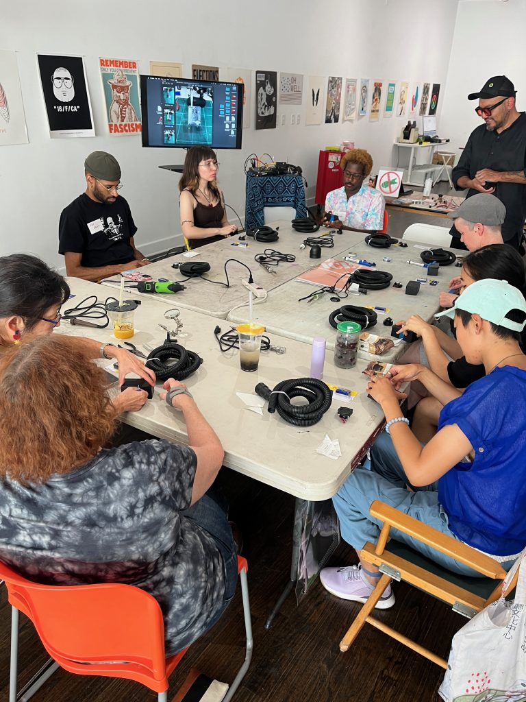 A photograph of eight attendees of the Vozu workshop working around tables with recycled materials in front of them. Courtesy of Co-Prosperity.