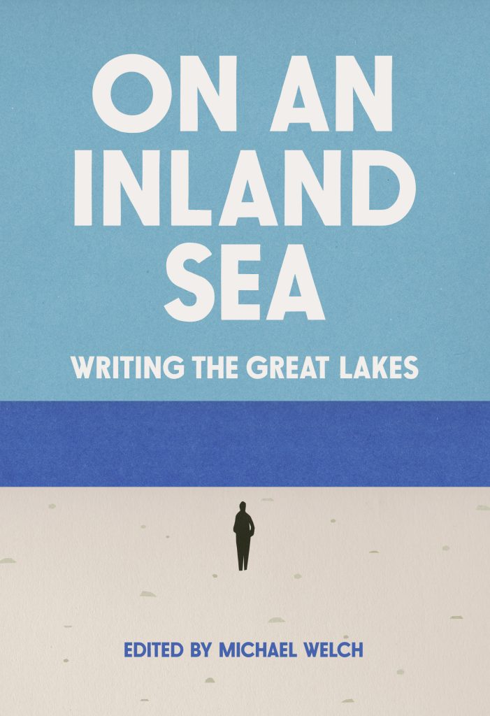 The book's cover art. In large, white letters the book's title, "ON AN INLAND SEA writing the Great Lakes" is centered over a light blue sky. Below that is a deep blue band representing the water. In the foreground, the silhouette of a person stands centered on a beach. At the bottom of the image is the text, "Edited by Michael Welch" in the same deep blue. Cover by David Wilson. Courtesy of Belt Publishing.