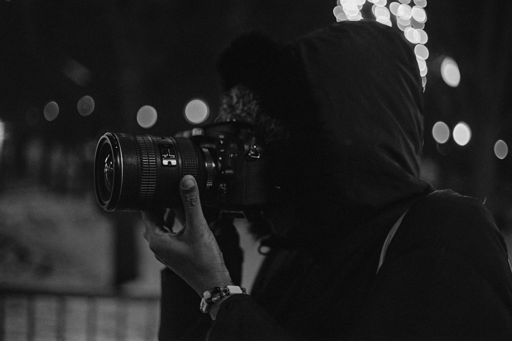A black and white capture of photographer Sam Wilson in profile, holding her camera to her face as if taking a photo. Photo by Genesis Falls.