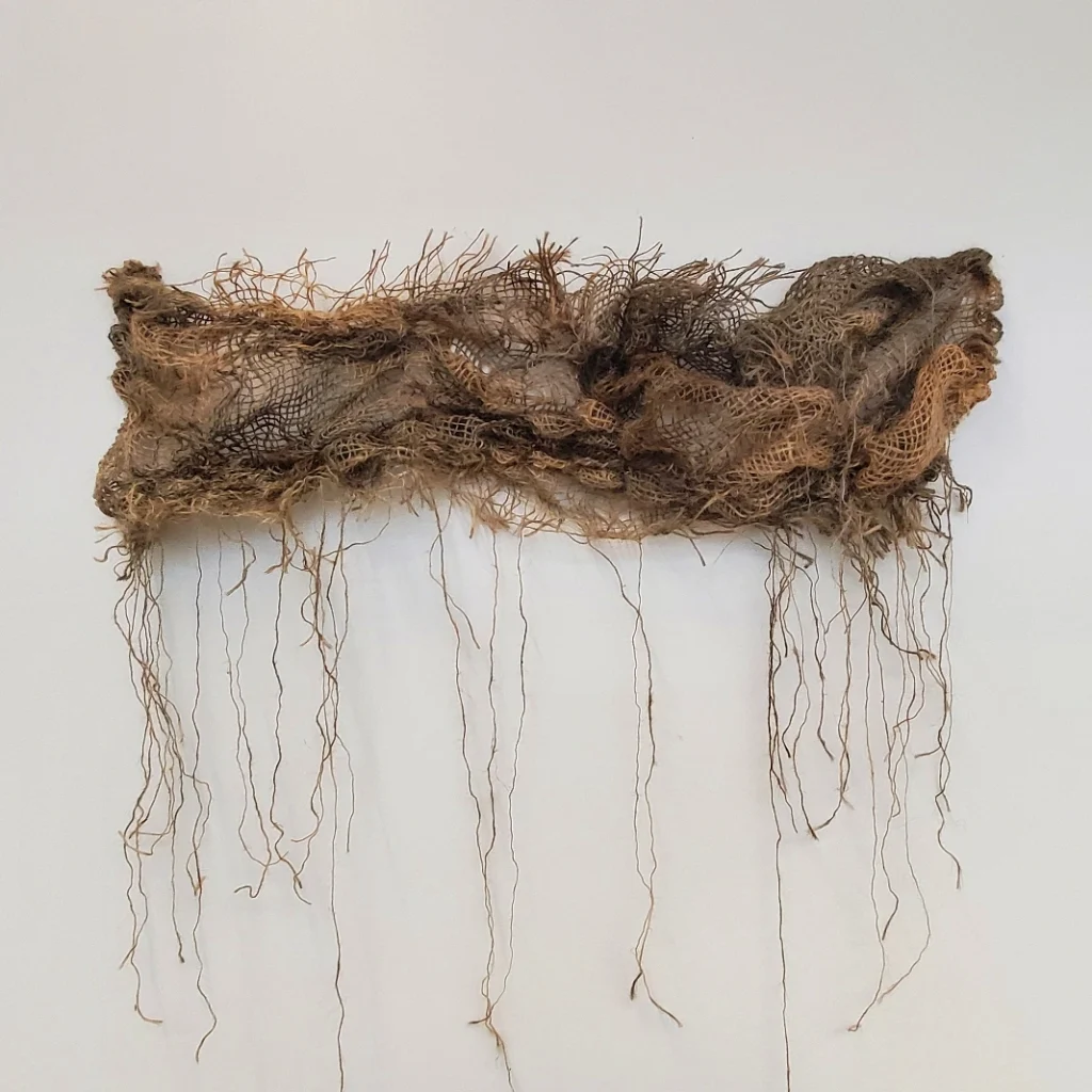 No Strings Attached, burlap, 2023. A horizonal burlap piece stained with oxidation of steel is hung on the gallery wall. Image courtesy of the artist.